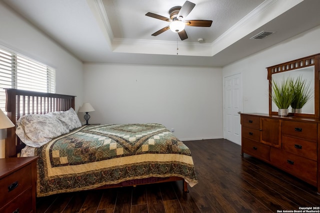 bedroom with a raised ceiling, ornamental molding, dark wood-type flooring, and visible vents