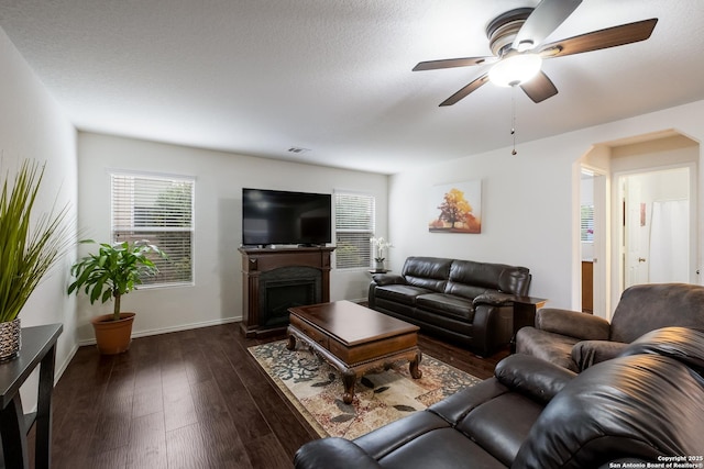 living room featuring a ceiling fan, dark wood-style floors, a wealth of natural light, and a fireplace