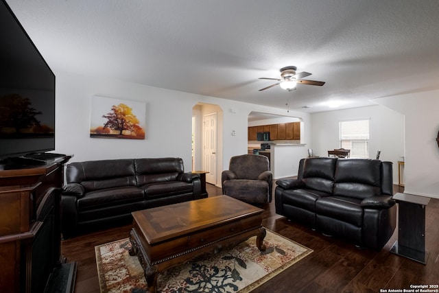 living area featuring dark wood-style flooring, a ceiling fan, and arched walkways