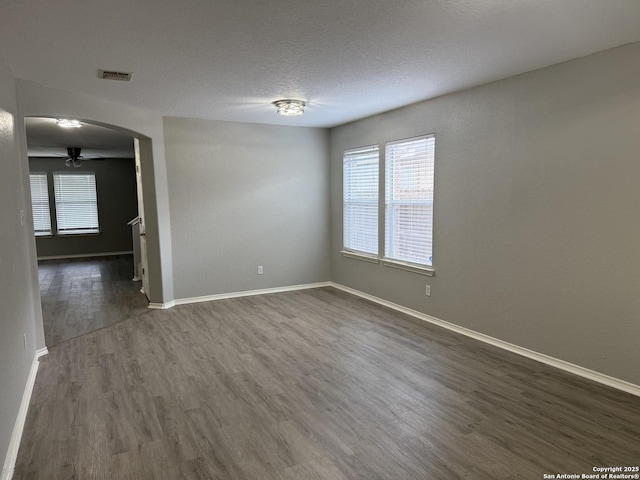 unfurnished room featuring baseboards, arched walkways, dark wood-style floors, and a wealth of natural light