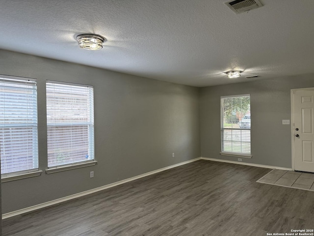 interior space featuring a textured ceiling, baseboards, wood finished floors, and visible vents