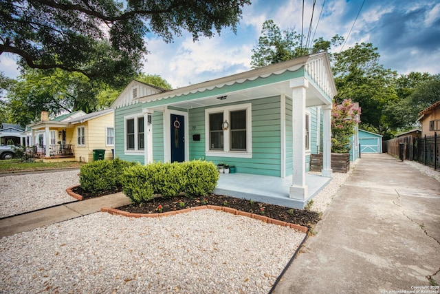 bungalow-style house with covered porch, board and batten siding, an outbuilding, a garage, and fence