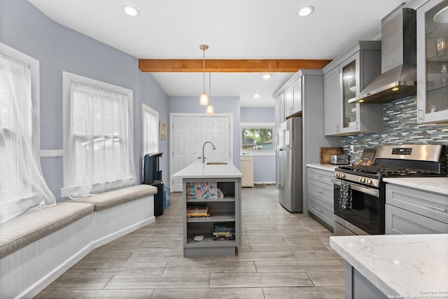 kitchen with a sink, wall chimney exhaust hood, stainless steel appliances, beamed ceiling, and gray cabinetry