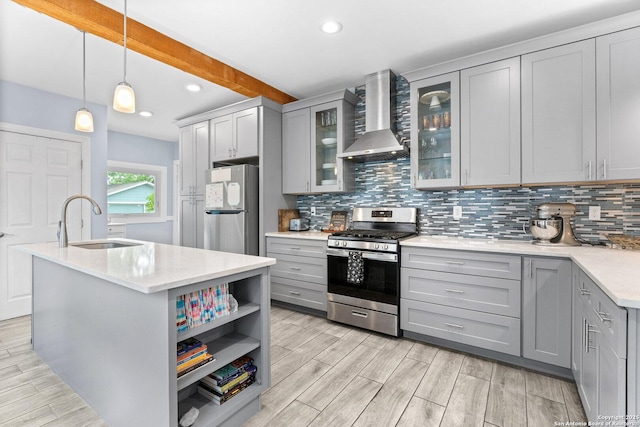 kitchen featuring appliances with stainless steel finishes, tasteful backsplash, gray cabinetry, a sink, and wall chimney exhaust hood
