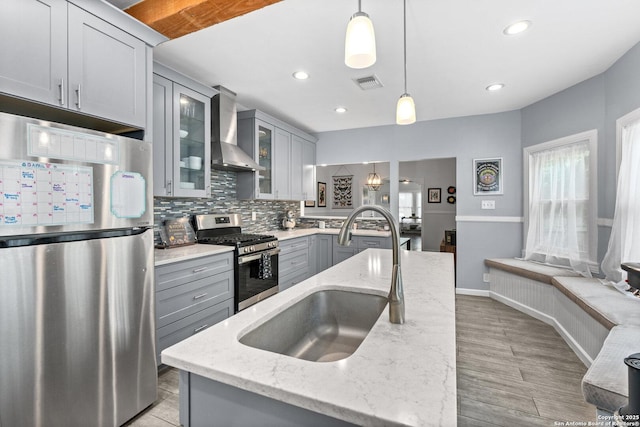 kitchen featuring gray cabinets, visible vents, a sink, stainless steel appliances, and wall chimney exhaust hood