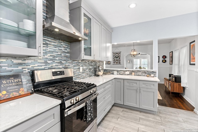 kitchen featuring wall chimney range hood, backsplash, stainless steel range with gas stovetop, a peninsula, and light wood-style floors