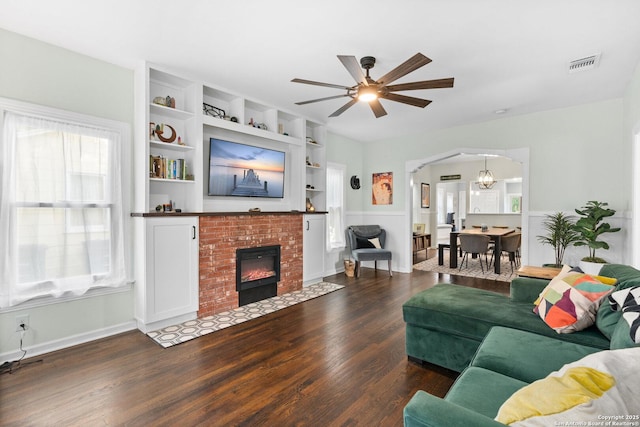 living area featuring ceiling fan, a brick fireplace, arched walkways, wood finished floors, and visible vents