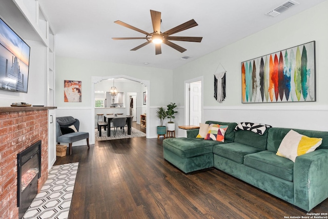 living area featuring a ceiling fan, visible vents, arched walkways, a fireplace, and wood finished floors
