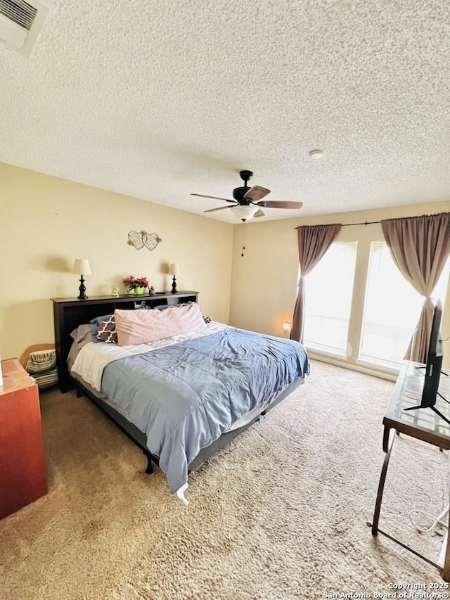 carpeted bedroom with a textured ceiling, visible vents, and ceiling fan