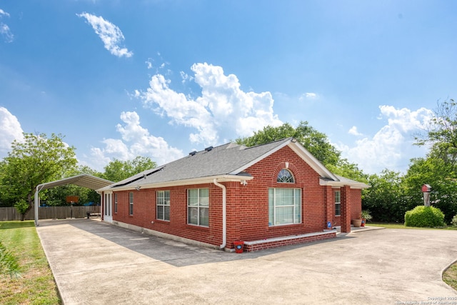 view of side of property featuring fence, a shingled roof, brick siding, concrete driveway, and a carport
