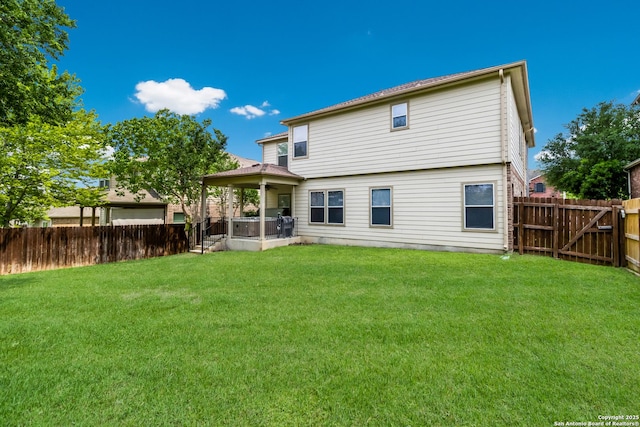 back of house with a fenced backyard, a hot tub, and a yard
