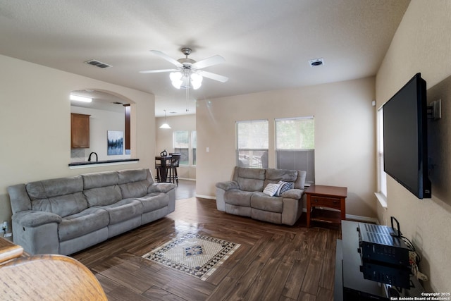 living room featuring a ceiling fan, arched walkways, visible vents, and baseboards