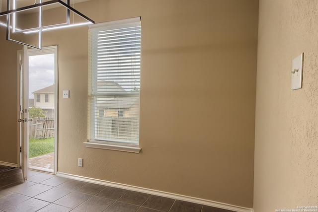 doorway with dark tile patterned floors, a textured wall, and baseboards