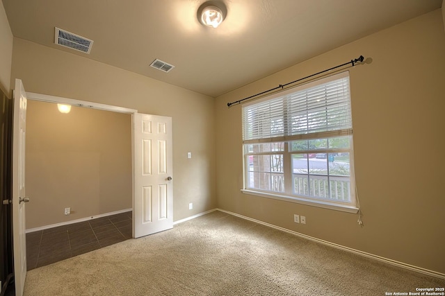 carpeted empty room with visible vents, baseboards, and tile patterned flooring
