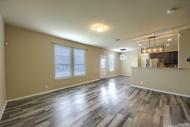 unfurnished living room featuring visible vents, dark wood-style flooring, and baseboards