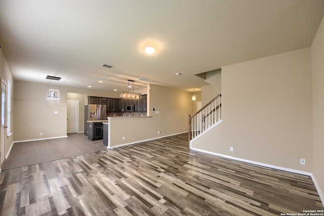 unfurnished living room featuring visible vents, stairs, baseboards, and wood finished floors