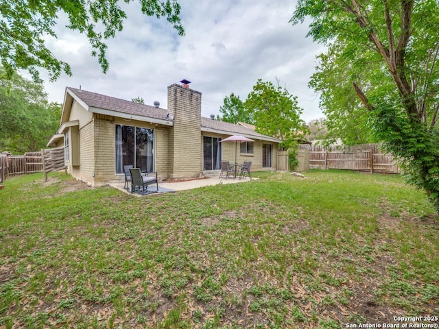 rear view of house featuring a fenced backyard, a chimney, brick siding, a patio area, and a yard