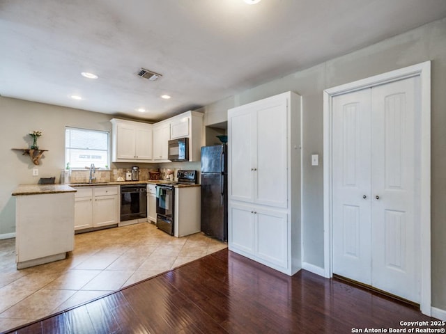kitchen with visible vents, baseboards, white cabinetry, a sink, and black appliances