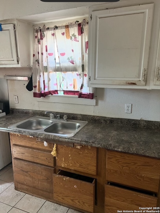 kitchen featuring a sink, light tile patterned flooring, white cabinets, and dark countertops