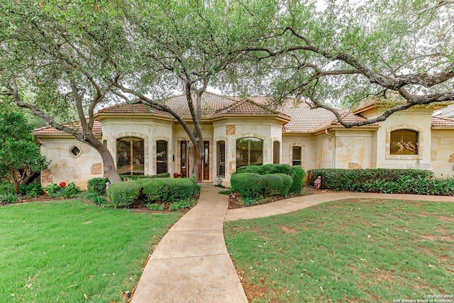 mediterranean / spanish-style house featuring stone siding, stucco siding, a tiled roof, and a front yard