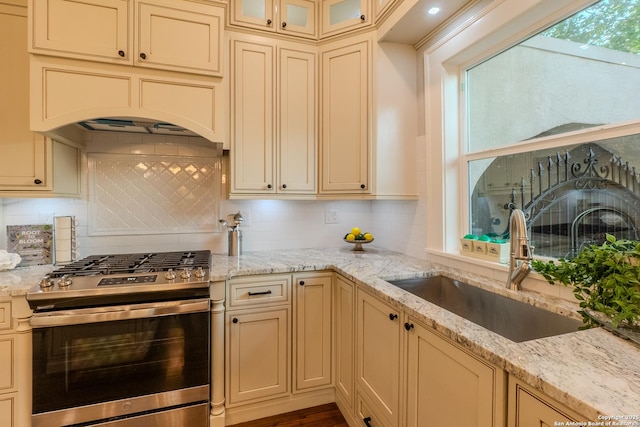 kitchen with stainless steel gas stove, cream cabinets, a sink, decorative backsplash, and light stone counters