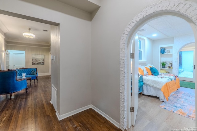 hallway featuring arched walkways, wood-type flooring, built in features, baseboards, and ornamental molding