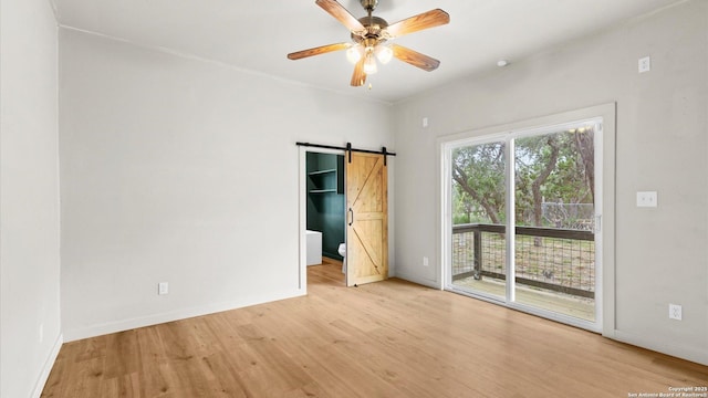 empty room featuring baseboards, a barn door, light wood-style flooring, and a ceiling fan