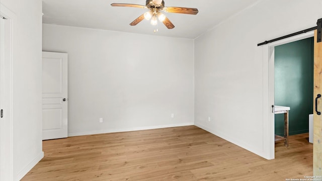 unfurnished room featuring baseboards, a barn door, light wood finished floors, and a ceiling fan
