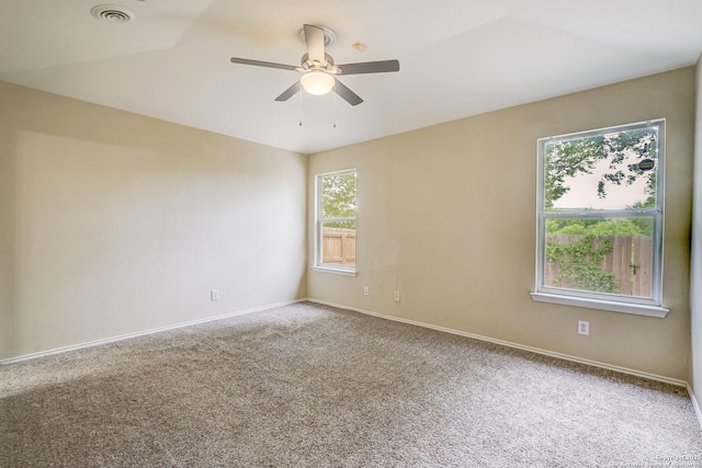 carpeted spare room featuring plenty of natural light, baseboards, ceiling fan, and visible vents