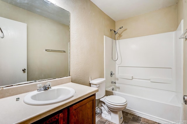 full bathroom featuring stone finish floor, vanity, toilet, a textured wall, and tub / shower combination