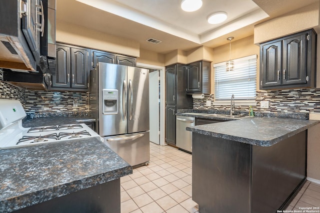 kitchen featuring visible vents, a peninsula, dark countertops, a sink, and appliances with stainless steel finishes
