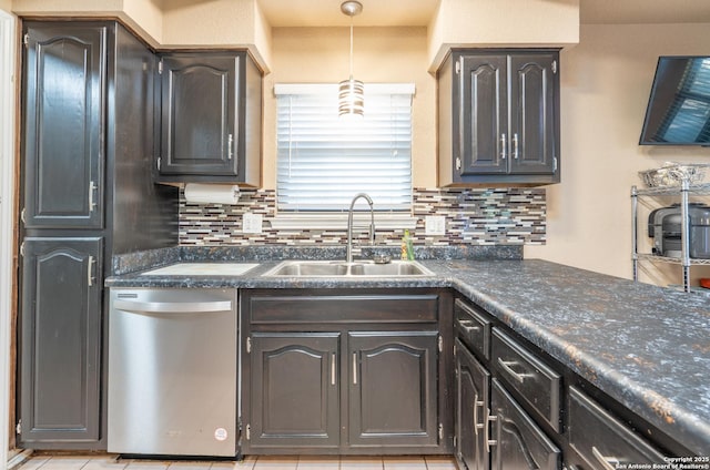 kitchen with stainless steel dishwasher, dark countertops, a sink, and tasteful backsplash