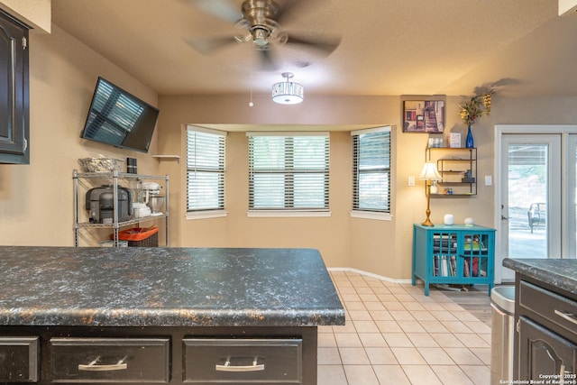 kitchen featuring baseboards, a ceiling fan, light tile patterned flooring, and dark countertops