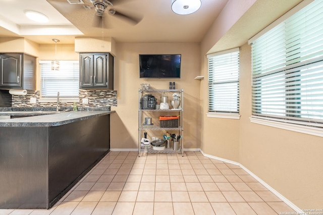 kitchen with light tile patterned flooring, dark countertops, ceiling fan, baseboards, and backsplash