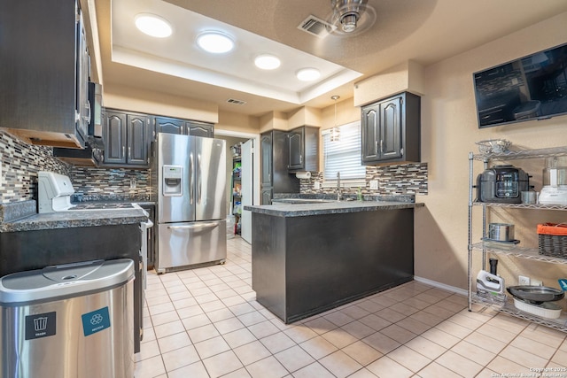 kitchen featuring dark countertops, a raised ceiling, stainless steel fridge with ice dispenser, decorative backsplash, and light tile patterned floors