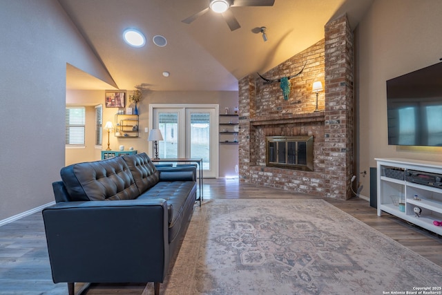 living area with a ceiling fan, a brick fireplace, wood finished floors, high vaulted ceiling, and baseboards