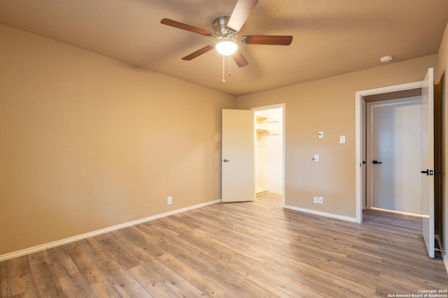 unfurnished bedroom featuring baseboards, ceiling fan, light wood-style flooring, and a walk in closet