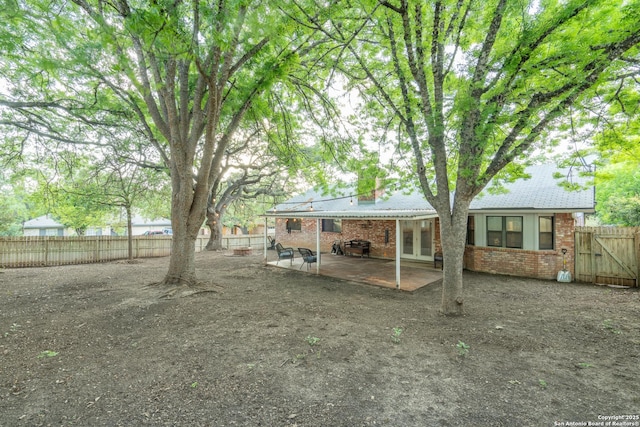 view of yard with a gate, french doors, a fenced backyard, and a patio area