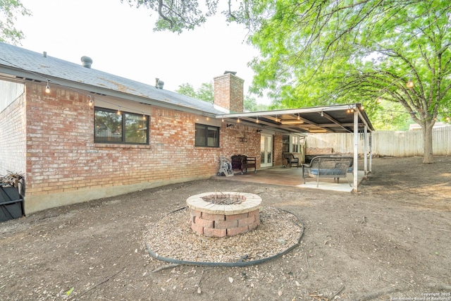 rear view of property featuring brick siding, fence, a fire pit, and a chimney