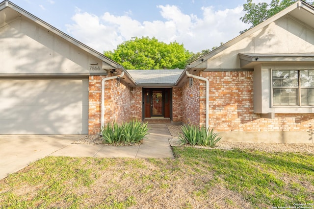 view of exterior entry featuring a garage, a yard, concrete driveway, and brick siding
