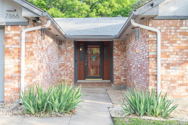 property entrance featuring brick siding and a shingled roof