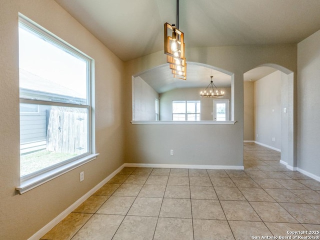 empty room with lofted ceiling, light tile patterned flooring, baseboards, a chandelier, and arched walkways