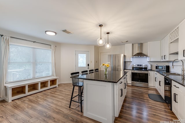 kitchen featuring a breakfast bar area, a kitchen island, a sink, stainless steel appliances, and wall chimney exhaust hood