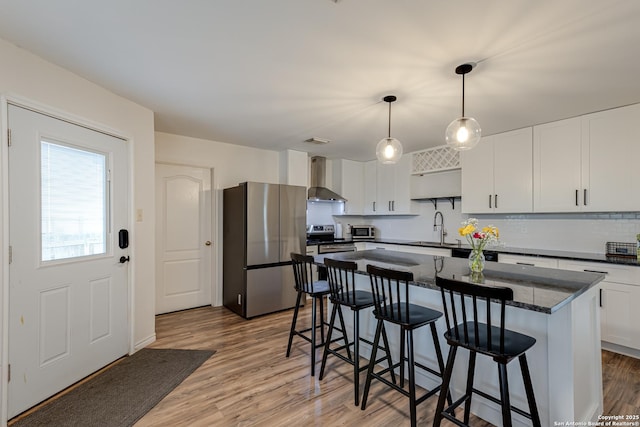 kitchen featuring stainless steel appliances, a breakfast bar, a sink, and wall chimney exhaust hood