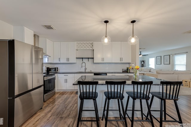 kitchen with a kitchen breakfast bar, visible vents, a center island, open floor plan, and stainless steel appliances