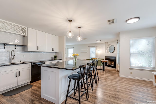 kitchen with black dishwasher, a center island, tasteful backsplash, a sink, and light wood-style flooring