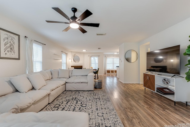 living area with baseboards, a ceiling fan, wood finished floors, and visible vents