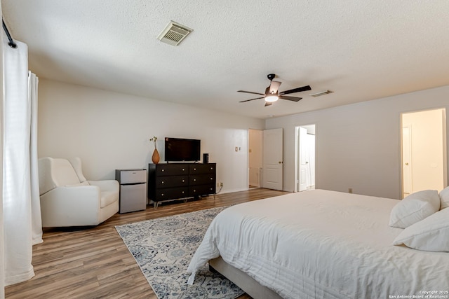 bedroom with a textured ceiling, ceiling fan, wood finished floors, and visible vents