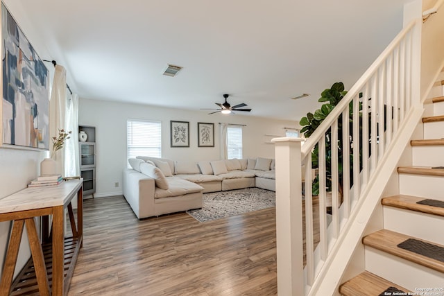 living area with visible vents, a ceiling fan, stairs, and wood finished floors