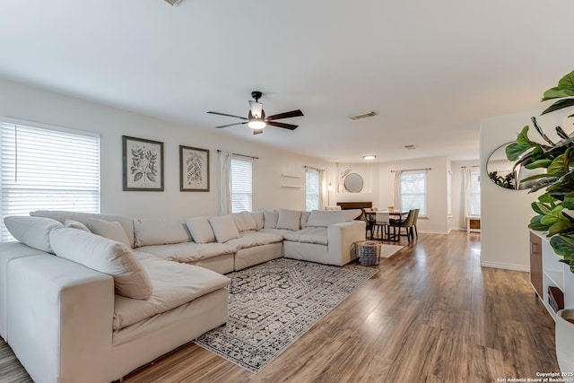 living area with a ceiling fan, baseboards, visible vents, and wood finished floors